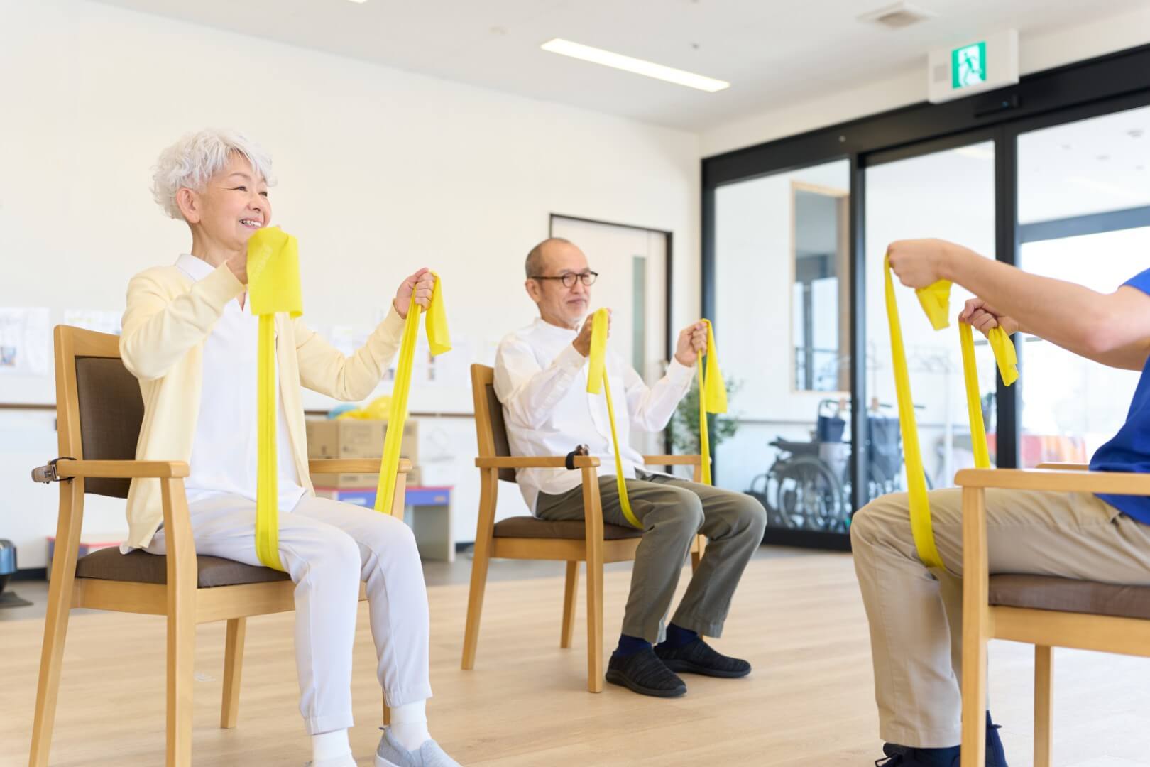Seniorinnen und Senioren turnen im Sesselkreis mit Gymnastikbändern